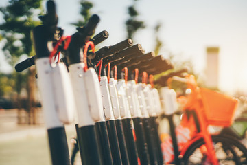 Urban electric transportation outdoors: the row of electric scooter bikes with batteries in the center, red electric bicycles behind, selective focus, Lisbon, Portugal © skyNext
