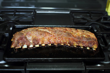Rack of dry rub pork ribs baked on a cast iron tray, resting on the stove top.