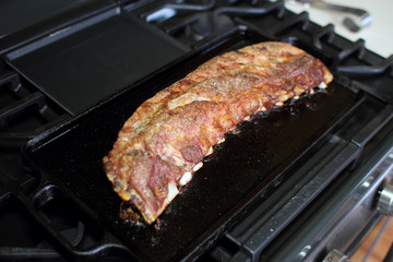 Rack of dry rub pork ribs baked on a cast iron tray, resting on the stove top.