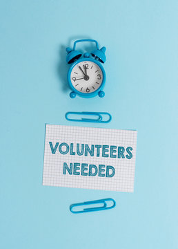 Handwriting text writing Volunteers Needed. Conceptual photo need work or help for organization without being paid Alarm clock wakeup squared blank paper sheet clips colored background