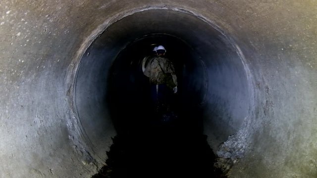 Sewer tunnel worker going through round sewer tunnel