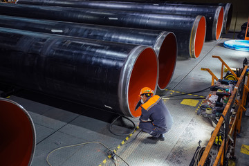 Worker examines new coated pipe in factory