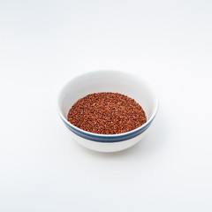 Red quinoa raw, bowl half full, on white background