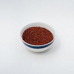 Red Quinoa raw on white background, bowl filed up to three fourths