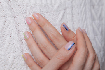 Nail polish. Art manicure. Modern style multi-collored nail polish. Stylish pastel color colored nails holding wool material sleeve blouse