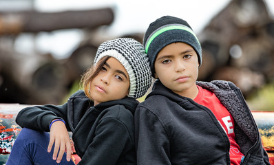 Portrait of boy and girl leaning on one another wearing hats outdoors