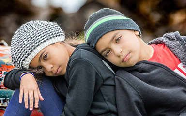 Portrait of boy and girl leaning on one another wearing hats outdoors