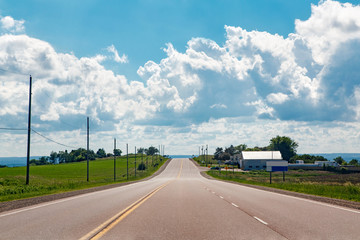 Beautiful landscape midday view of Canadian Ontario empty countryside road during sunny day with white clouds in blue sky. Outdoor country village street with nobody at summer.
