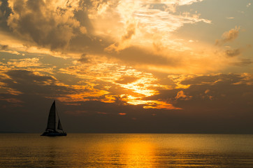 Sailing boat (sailboat, yacht) during the beautiful, orange and cloudy sunset