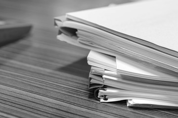 Pile of unfinished paperwork stacked in archive with plastic slide binder bars waiting to be managed and inspected for score and laptop nearby. Report papers stacks. Business and education concept.