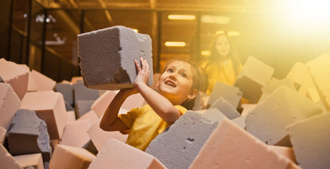 Little happy girls play and have fun in a dry pool with paralon cubes in a children's entertainment...