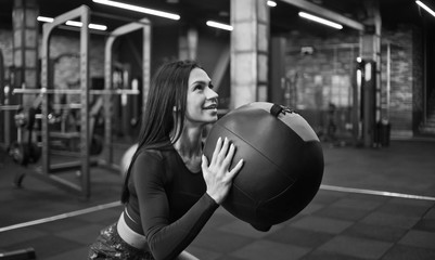Cheerful brunette woman in sportswear doing exercise with medicine ball.