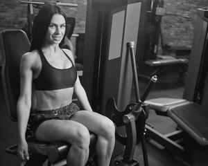 Fototapeta na wymiar Attractive brunette in sportswear sitting in exercise machine and looking into the camera