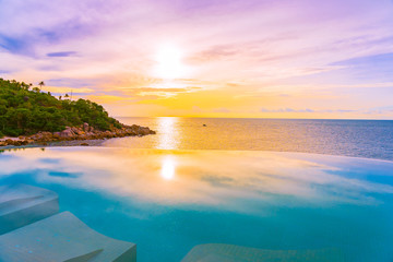 Fototapeta na wymiar Beautiful outdoor infinity swimming pool with coconut palm tree around beach sea ocean at sunrise or sunset time