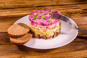White plate with russian traditional new year salad herring under fur coat and rye bread on wooden table