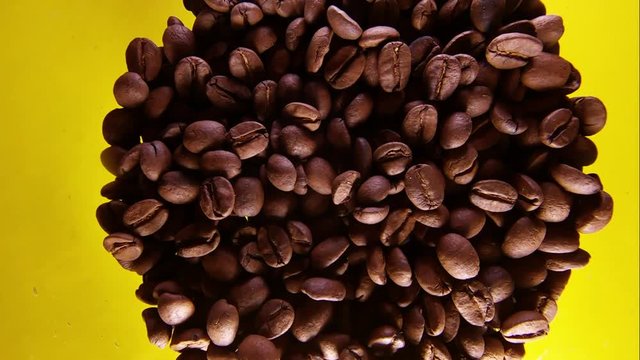 Slow Motion Of Mixing Coffee Beans In A Glass Isolated On Yellow Bacground.