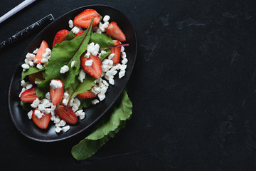 Salad with fresh strawberry, cottage cheese and beet leaves, flatlay with copyspace over black stone background