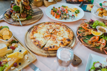 Dinner table with variety food, pizza, seafood and sushi