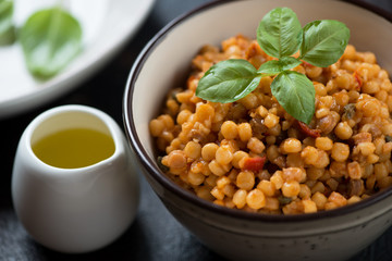 Close-up of fregola pasta with bell pepper, capers, fresh green basil and olive oil, selective focus