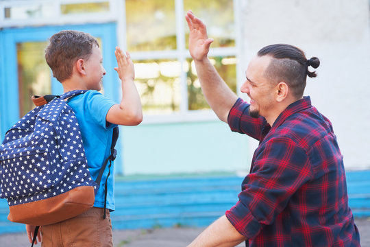 Back To School.Happy Father And Son Are Welcome Before Elementary School. Parent Meets A Child From Elementary School.The Student Goes To School With A Backpack.