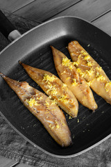 Smoked mackerel in a griddle frying pan with grated lemon peel on top.  With selective colour