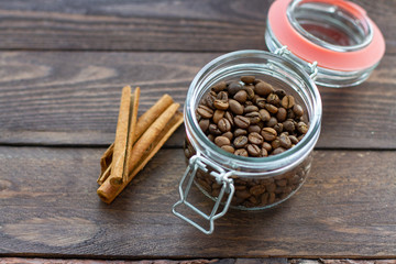 coffee beans in glass jars and cinnamon sticks on wooden background