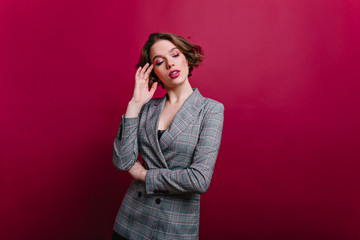 Pensive business-woman with pink makeup posing on claret background. Serious young lady in gray...