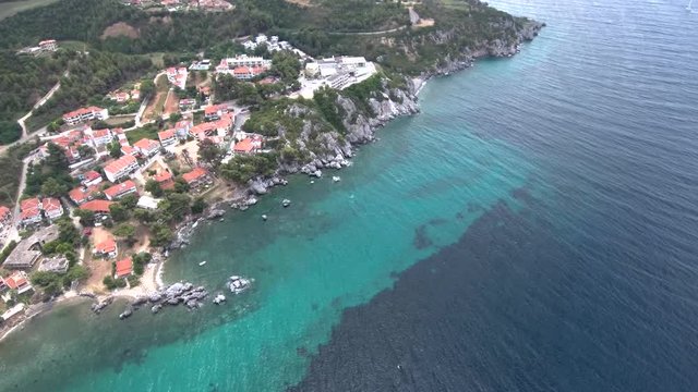 Aerial view of small turquoise beach with rocks under a tourist village in the area of Agia Paraskevi Halkidiki, Greece, circular movement by drone