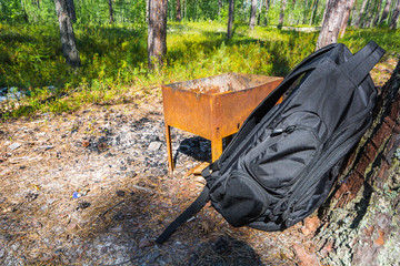 Black sports backpack costs about rusty barbecue in the forest.