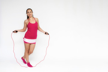 Full-length portrait on white background of beautiful pretty fitness girl woman in pink sport uniform standing exercises in different poses with a skipping rope. Smiles Stylish trendy youth.