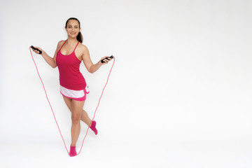 Full-length portrait on white background of beautiful pretty fitness girl woman in pink sport uniform standing exercises in different poses with a skipping rope. Smiles Stylish trendy youth.