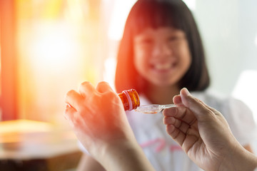 Happy Asia little child girl smiling want to take medicine form mother. Asian kid female waiting to eat drug. Hands of mom pouring cough syrup medicine into clear spoon to daughter.