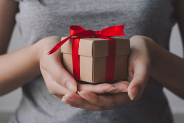 Close up of woman hand holding small brown gift box wrapped with red ribbon.
