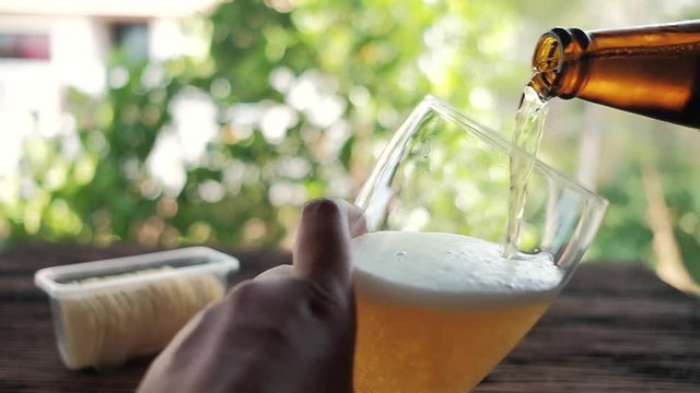 Slow Motion of Young Person Pouring Beer from Bottle into a Glass at the Backyard. POV Shot