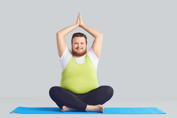 Positive fat man Yogi does yoga exercises a gray background.
