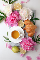 Morning cup of tea and fresh beautiful pink and white peony flowers on white background. Top view. Flat layout, concept of female holiday morning, stylish blogger