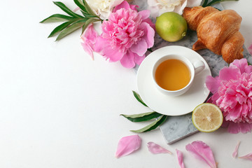 Obraz na płótnie Canvas Cup of tea, citrus with fresh flowers peonies on white background. Holiday feminine breakfast, celebration morning concept. Top view. Copy space.