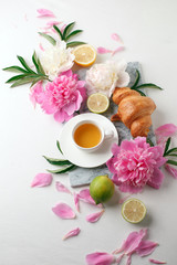 Fototapeta na wymiar Cup of tea, citrus with fresh flowers peonies on white background. Holiday feminine breakfast, celebration morning concept. Top view. Copy space.