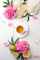 Fototapeta na wymiar Cup of tea, citrus with fresh flowers peonies on white background. Holiday feminine breakfast, celebration morning concept. Top view. Copy space.