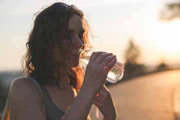 brunette girl with water in glass bottle in park