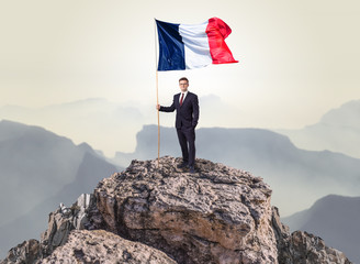 Successful businessman on the top of a mountain holding France victory flag