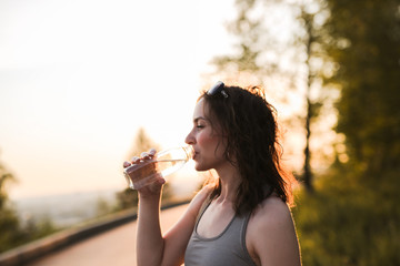 brunette girl with water in glass bottle in park