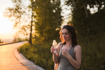 brunette girl with water in glass bottle in park