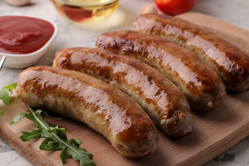 Delicious grilled sausages on a board with red sauce and spices on a light background. B-B-Q.