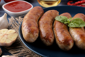 Delicious grilled sausages on a plate with red sauce and spices on a blue wooden background. B-B-Q.