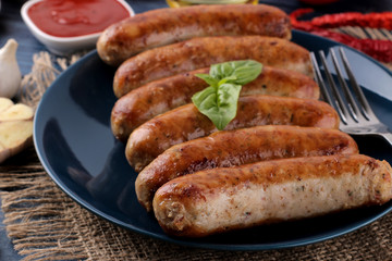 Delicious grilled sausages on a plate with red sauce and spices on a blue wooden background. B-B-Q.