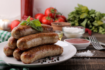 Delicious grilled sausages on a plate with red sauce and spices on a brown wooden background. B-B-Q.