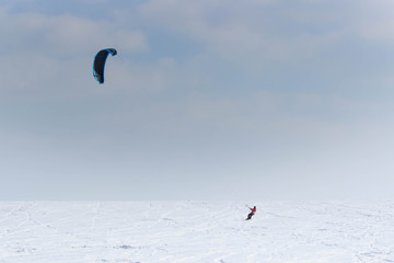 A snowboarder with a kite rides on a frozen lake on free ride.