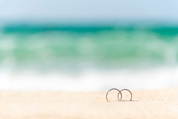 Fototapeta na wymiar Couple engagement wedding rings on summer tropical sand beach with copy space. Display design for honeymoon travel agency concept. Wedding rings on sand with holiday vacation for couple propose marry