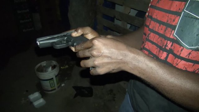 KINGSTON, JAMAICA : Jamaican young gang holding hand gun with bullet in dark alley at night.